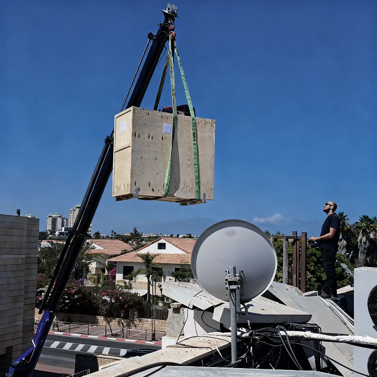 טכנאי קירור עומד על הגג לצד מנוף בעת החלפת יחידת קירור