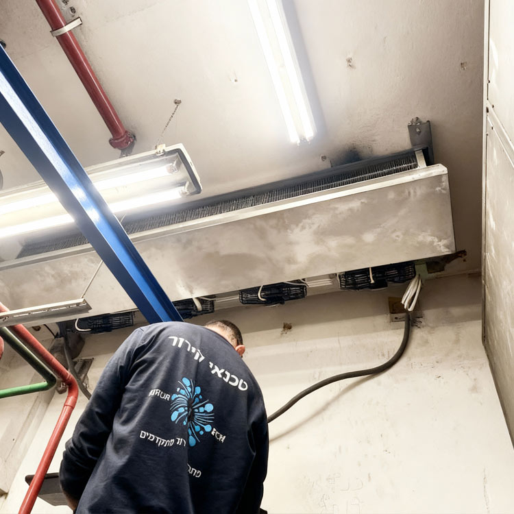 טכנאי קירור עומד על סולם מחליף מפזר בחדר מכונות